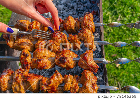 A girl using a fork checks the readiness of the kebab marinated meat on skewers on the grill 78146269