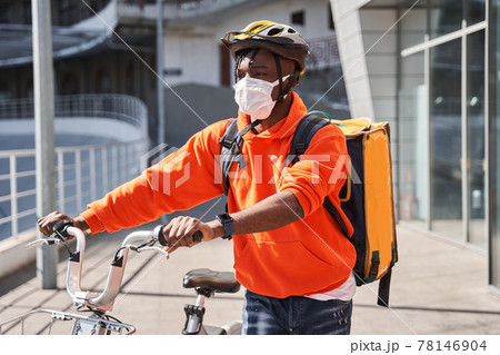 Man wearing helmet with a backpack crossing the road with a bicycle 78146904