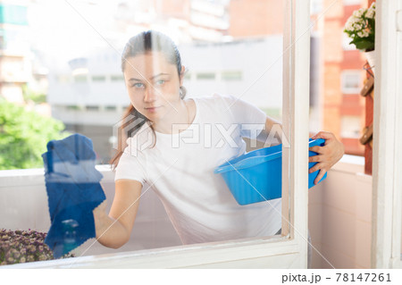 Young positive woman doing chores cleaning window Young positive woman doing chores cleaning window 78147261