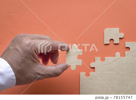 Man's hand inserting piece of puzzle into the jigzaw puzzle on table. 78155747