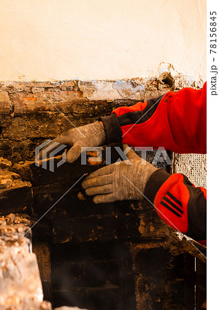 Man destroys an old brick stove, black brick in soot, dismantling the old kitchen surface. 78156845