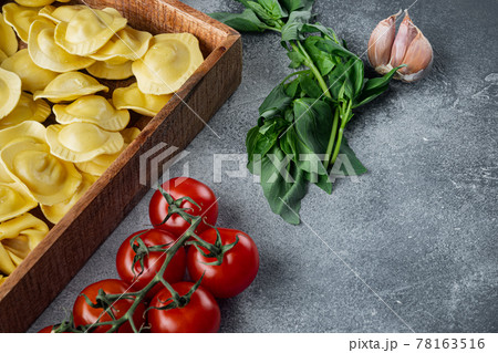 Italian raw handmade Ravioli with fresh ingredients, basil, pesto, ham, mozzarella cheese, parmesan, in wooden box, on gray background, with copy space for text 78163516