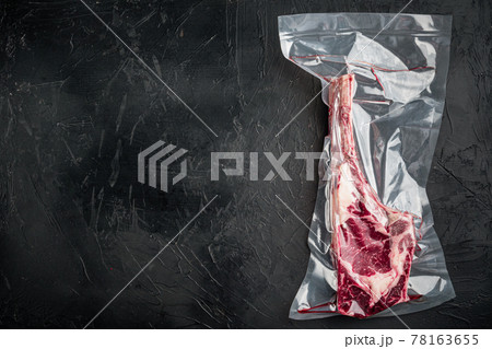 Bone Tomahawk Steak in vacuum commercial pack, on black stone background, top view flat lay, with copy space for text Bone Tomahawk Steak in vacuum commercial pack, on black stone background, top view flat lay, with copy space for text 78163655