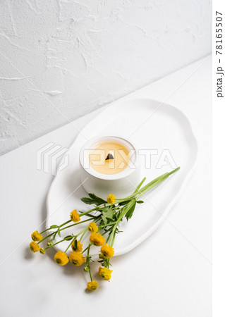 White burning candle with wooden wick and yellow flowers on white tray White burning candle with wooden wick and yellow flowers on white tray 78165507