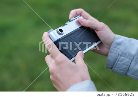 Female hands holding retro photo camera and taking snapshots on background grass. Female hands holding retro photo camera and taking snapshots on background grass. 78166925