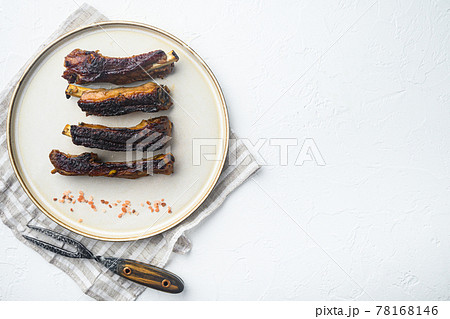 Spicy hot grilled spare ribs from a summer BBQ, on plate, with barbeque knife and meat fork, on white stone background, top view flat lay, with copy space for text 78168146
