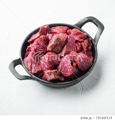 Raw ingredients for goulash. Fresh raw chopped beef, in cast iron frying pan, on white stone surface, square format Raw ingredients for goulash. Fresh raw chopped beef, in cast iron frying pan, on white stone surface, square format 78168319