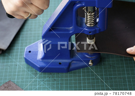 Artisan using hand press for setting snaps in leather for makes a wallet. Hand Pressure Snap Pressing Machine is using by craftsman in leather workshop. 78170748
