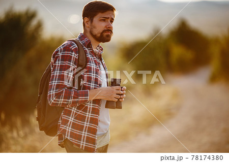 Guy looking at binoculars in hill. man in t-shirt with backpack. Guy looking at binoculars in hill. man in t-shirt with backpack. 78174380