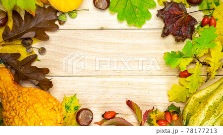 Autumn pattern. Natural harvest with orange pumpkin, fall dried leaves, red berries and acorns, chestnuts on wooden background in shape frame. Autumn Thanksgiving day background. 78177213
