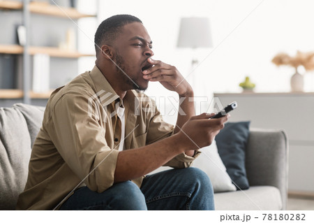Bored Black Guy Yawning Watching TV Sitting On Couch Indoors Bored Black Guy Yawning Watching TV Sitting On Couch Indoors 78180282