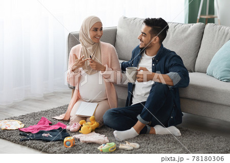 Pregnant Islamic Spouses Preparing Baby Clothes At Home, Making Checklist Of Necessities 78180306