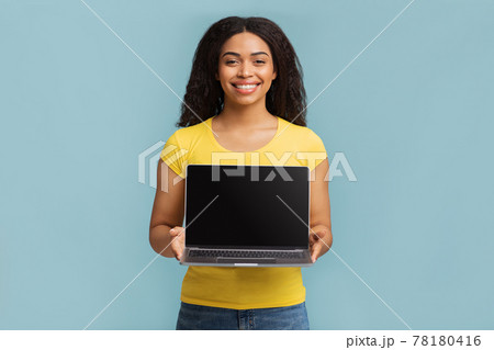 Positive black woman holding and showing laptop computer with black empty screen for mockup, blue background Positive black woman holding and showing laptop computer with black empty screen for mockup, blue background 78180416