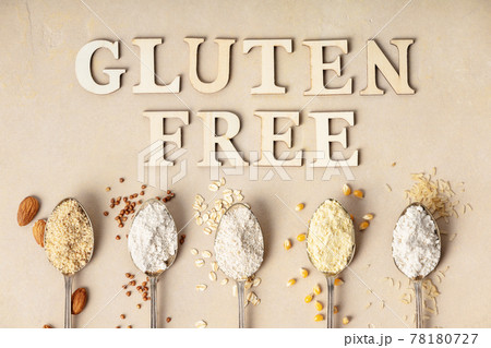 Metal spoons of various gluten free flour almond flour, oatmeal flour, buckwheat flour, rice flour, corn flour and gluten free lettering made of wooden letters, flat lay, top view 78180727