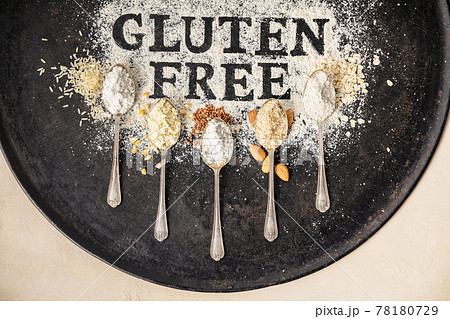 Gluten free written in flour on vintage baking sheet and spoons of various gluten free flour almond flour, buckwheat flour, rice flour, corn flour, oatmeal flour , flat lay, top view 78180729