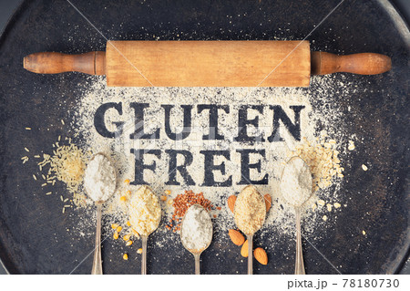 Gluten free written in flour on vintage baking sheet, rolling pin and spoons of various gluten free flour almond flour, buckwheat flour, rice flour, corn flour, oatmeal flour , flat lay, top view 78180730