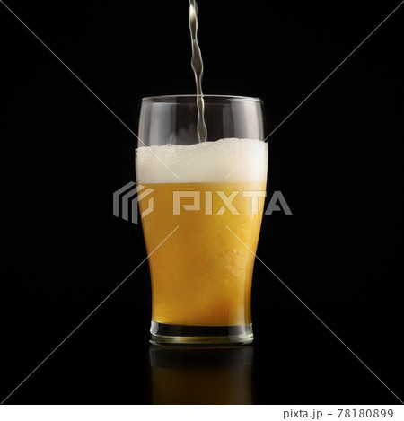 Jet of fresh light beer is poured into glass goblet on dark background with splashes and foam 78180899