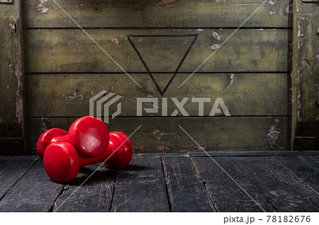 Red dumbbells for fitness in a dark room. Women's dumbbells in the military hall. Copy space. Red dumbbells for fitness in a dark room. Women's dumbbells in the military hall. Copy space. 78182676