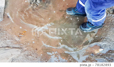 Close-up of a child's feet in rubber boots, a boy child happily playing with a shovel in a muddy puddle with snow and ice, in the early spring in the yard Close-up of a child's feet in rubber boots, a boy child happily playing with a shovel in a muddy puddle with snow and ice, in the early spring in the yard 78182893