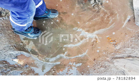 Close-up of a child's feet in rubber boots, a boy child happily playing with a shovel in a muddy puddle with snow and ice, in the early spring in the yard Close-up of a child's feet in rubber boots, a boy child happily playing with a shovel in a muddy puddle with snow and ice, in the early spring in the yard 78182894