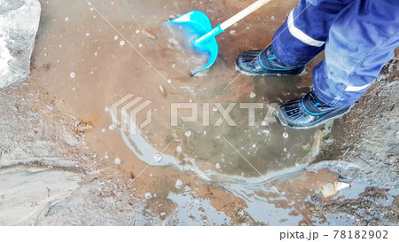 Close-up of a child's feet in rubber boots, a boy child happily playing with a shovel in a muddy puddle with snow and ice, in the early spring in the yard Close-up of a child's feet in rubber boots, a boy child happily playing with a shovel in a muddy puddle with snow and ice, in the early spring in the yard 78182902