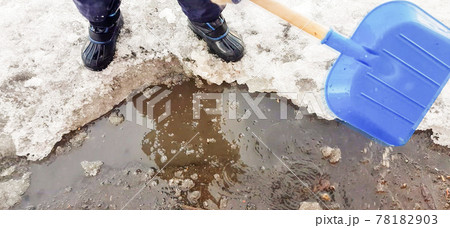 Close-up of a child's feet in rubber boots, a boy child happily playing with a shovel in a muddy puddle with snow and ice, in the early spring in the yard 78182903
