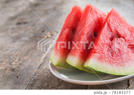 three slices of watermelon on a white plate on a wooden background 78183377