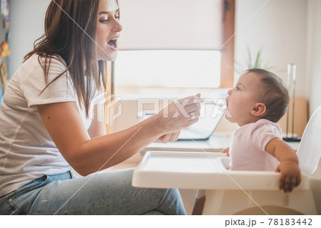 Mother feed her little daughter with a spoon Mother feed her little daughter with a spoon 78183442
