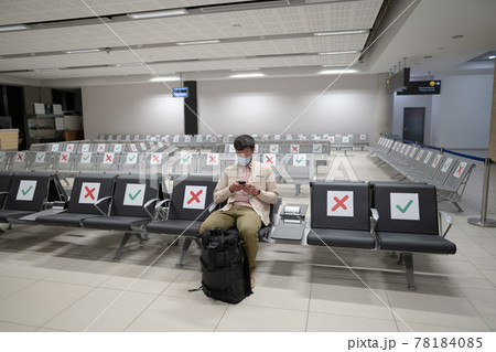 Waiting for flight at empty airport in Cyprus. Man sitting on chair with social distance marker at empty Paphos terminal. Flights canceled during quarantine. Collapse of airlines at coronavirus Waiting for flight at empty airport in Cyprus. Man sitting on chair with social distance marker at empty Paphos terminal. Flights canceled during quarantine. Collapse of airlines at coronavirus 78184085