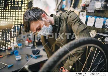 Mechanic repairs bicycle in workshop wearing covid 19 mask. Worker of bicycle store fixes bike during coronavirus quarantine in protective mask. Repairman maintenance cycle. Sport shop concept 78184086