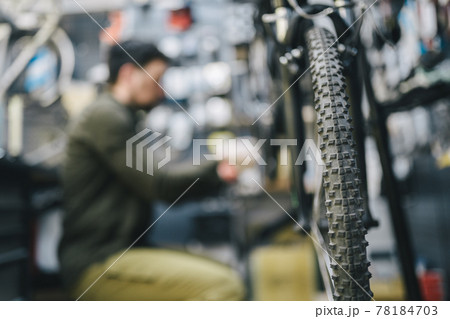 Mechanic repairs bicycle in workshop wearing covid 19 mask. Worker of bicycle store fixes bike during coronavirus quarantine in protective mask. Repairman maintenance cycle. Sport shop concept 78184703