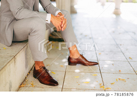 A man in a gray suit and leather brown shoes sits on the step with his hands folded A man in a gray suit and leather brown shoes sits on the step with his hands folded 78185876