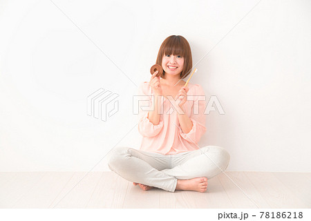 おやつと歯ブラシを手に胡座をかいて座る若い女性 78186218
