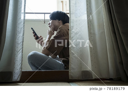 ベランダでスマホを見る男性 78189179