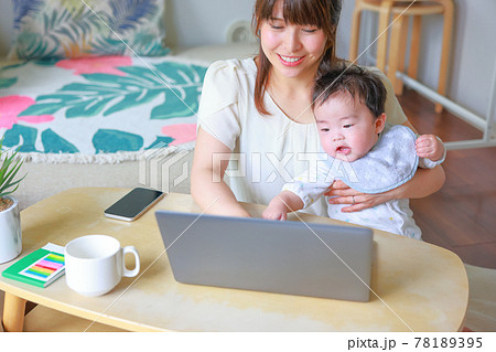 テレワークする母親にだっこされてpcに手を伸ばす乳児の写真素材