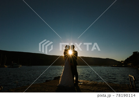 Groom and bride hold hands at sunset standing on the seashore Groom and bride hold hands at sunset standing on the seashore 78190114