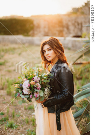 Serious bride in a pastel dress and black leather jacket with a bouquet of beautiful roses on a garden background Serious bride in a pastel dress and black leather jacket with a bouquet of beautiful roses on a garden background 78190157