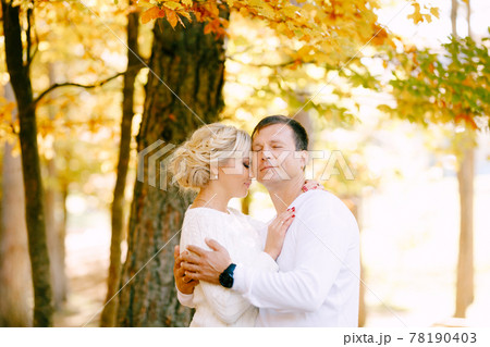 Half-length portrait of a man and a woman in white sweaters hugging against the background of trees in the autumn forest Half-length portrait of a man and a woman in white sweaters hugging against the background of trees in the autumn forest 78190403