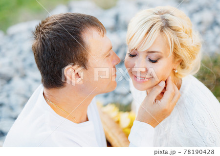 Man touches his hand to the cheek of closed-eyed woman while sitting on a blanket Man touches his hand to the cheek of closed-eyed woman while sitting on a blanket 78190428