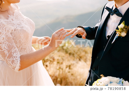 Bride in a beautiful dress puts a ring on the groom's finger 78190858