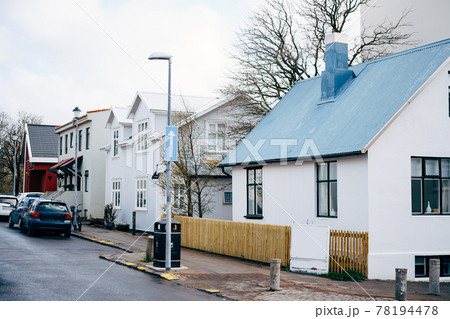 The facades of houses on the street in Reykjavik, the capital of Iceland. Several two-story houses and parked cars along the road. 78194478