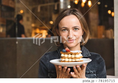 A beautiful caucasian woman holding and showing a plate with dessert in cafe 78195715