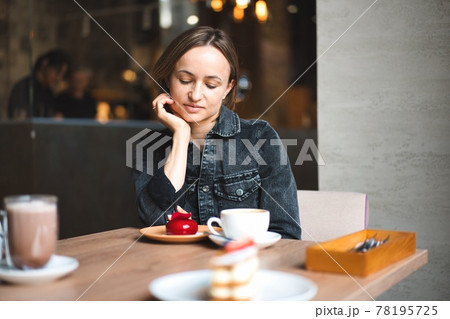 Portrait of a happy woman eating a piece of cake and drinking coffee while sitting at the table in a 78195725