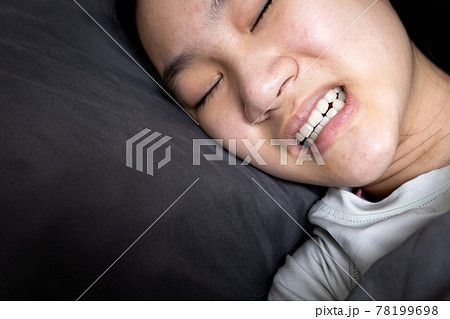 Asian child girl suffering from bruxism while lying in bed at night,female grinding of the teeth during sleep,teeth clenching,sleep disorders,oral health problems,dental care medical,bruxism concept 78199698