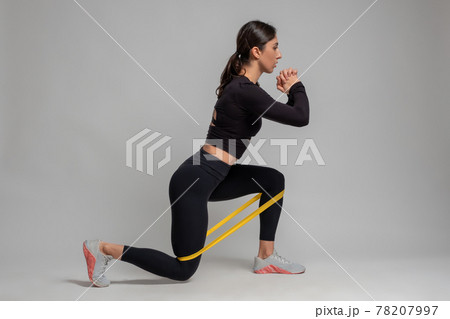Girl doing lunge with resistance band on grey background Girl doing lunge with resistance band on grey background 78207997