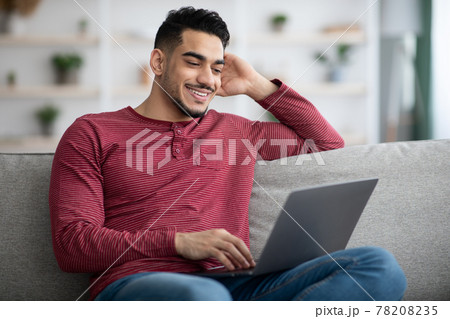Happy arab guy using laptop, chatting on dating website Happy arab guy using laptop, chatting on dating website 78208235