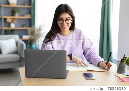 Woman sitting at desk, using computer writing in notebook Woman sitting at desk, using computer writing in notebook 78208380