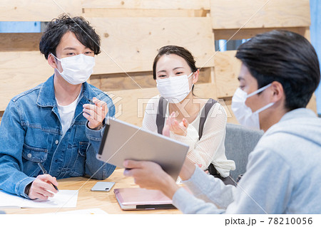 オフィスでマスクをしながらミーティングをするマ若い男女3人 78210056