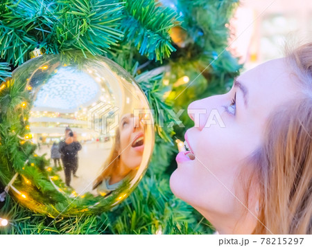 The girl's face looking up and her reflection in a golden ball hanging on the tree The girl's face looking up and her reflection in a golden ball hanging on the tree 78215297