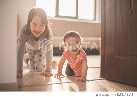 Girl play with her little sister at home. They have fun when walk on all fours Girl play with her little sister at home. They have fun when walk on all fours 78217373